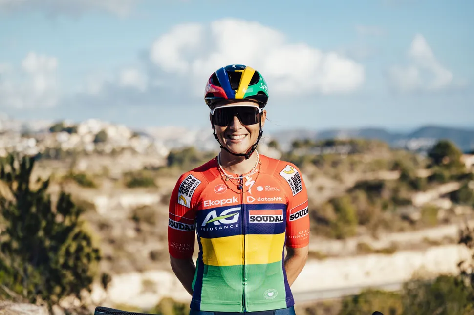 Cyclist in colorful gear smiling outdoors with a scenic background.